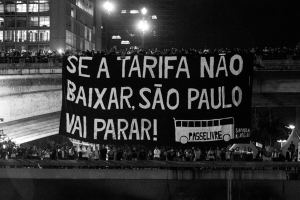 No dia 6 de junho de 2013 o Movimento Passe Livre bloqueou a Av. 23 de Maio com uma barricada de catracas de papel pegando fogo. Ao fundo, do alto do Viaduto do Chá ao Vale do Anhangabaú, o movimento posicionou uma enorme bandeira com a frase “SE A TARIFA NÃO BAIXAR SÃO PAULO VAI PARAR”. À direita estava o prédio da prefeitura de São Paulo. No dia seguinte esta cena foi capa do jornal Folha de S. Paulo, em uma imagem do fotógrafo Nelson Antoine. Aqui estamos publicando outra imagem, de autoria desconhecida, que mostra o bandeirão. (Graziela Kunsch)